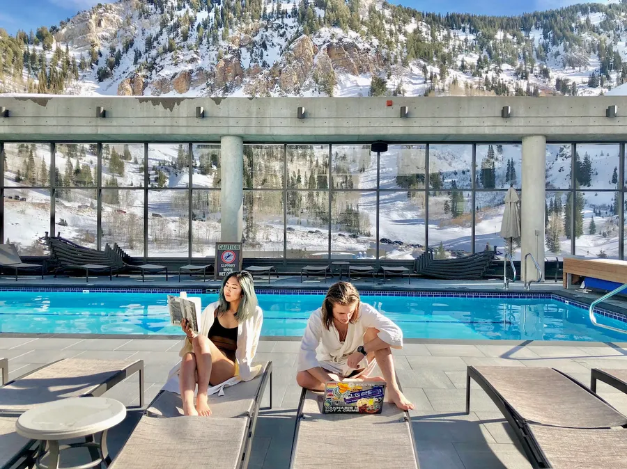 Jade Allen Cook and Mai Abe sitting at a rooftop pool with snow-covered mountains in the background.